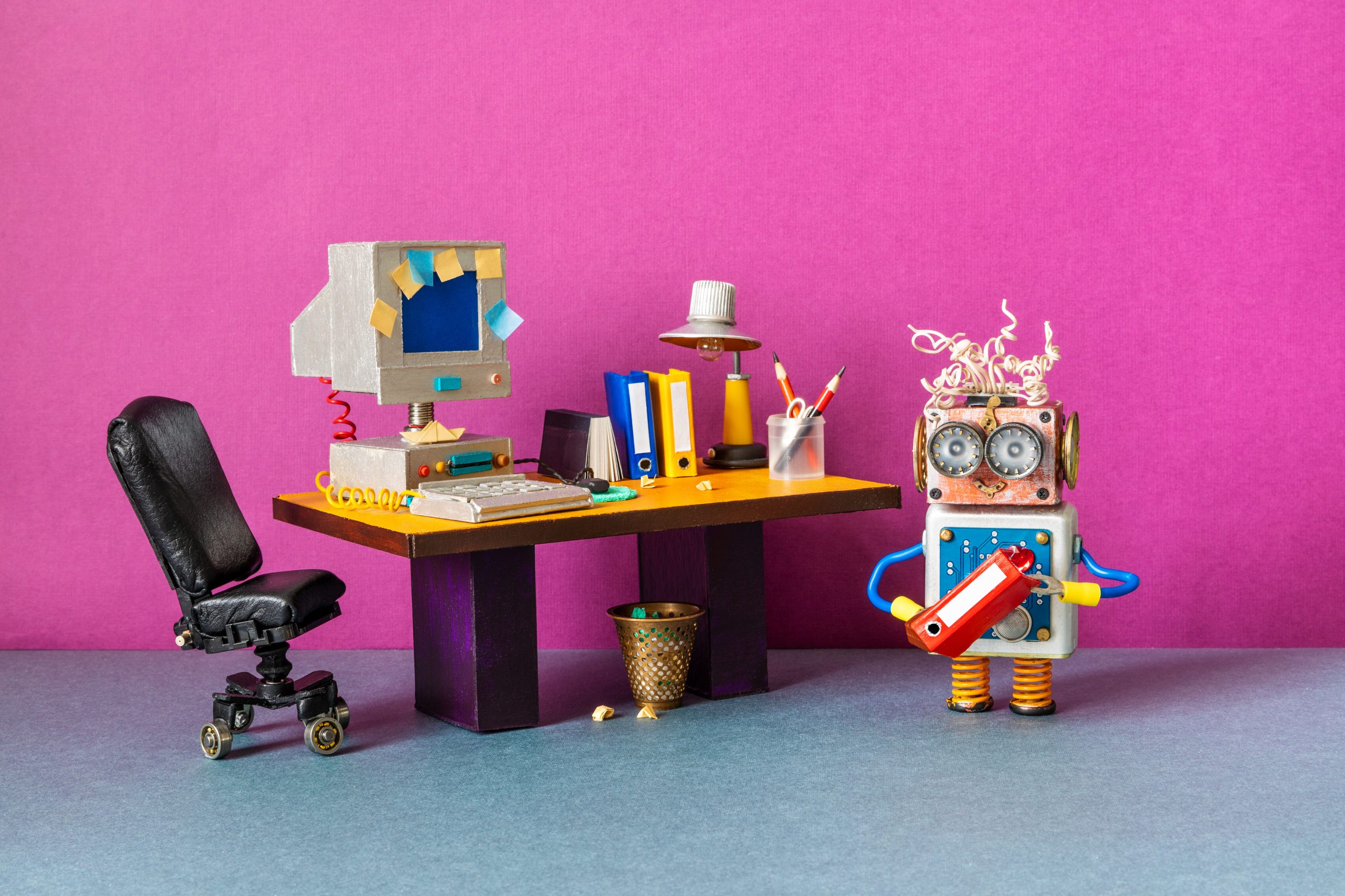 A funny robot office manager holds a folder with documents. Retro office with a computer and a desk lamp on an old table. The concept of workflow business automation. pink background
