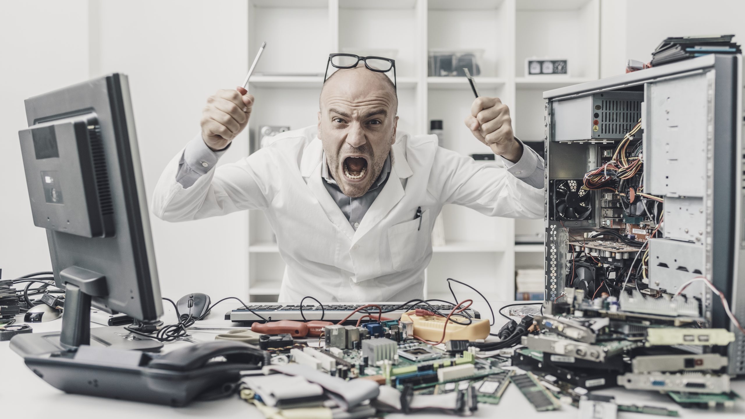 Frustrated angry technician trying to repair a computer, his desk is full of computer parts